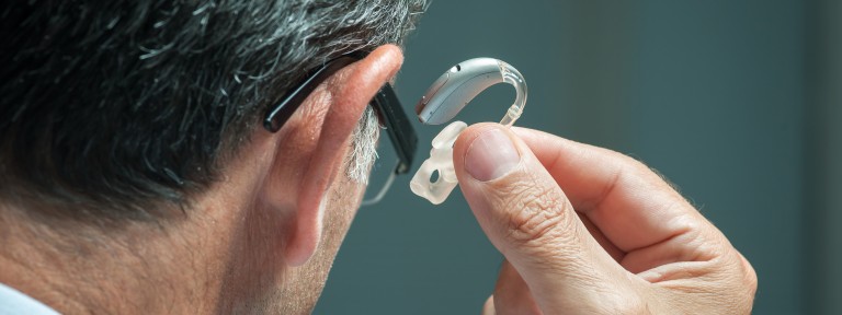 Älterer Mann hält Hörgerät neben sein Ohr