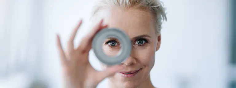 Frau hält eine Rolle vor ihr Gesicht und schaut mit einem Auge durch