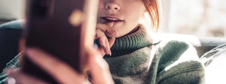 Junge rothaarige Frau schaut auf ihr Smartphone