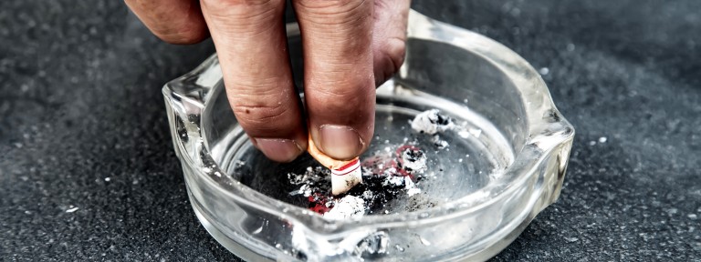 Männliche Hand drückt eine Zigarette im Aschenbecher aus