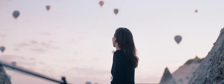 Frau blickt von Berg hinab und sieht einige Heißluftballons am Himmel