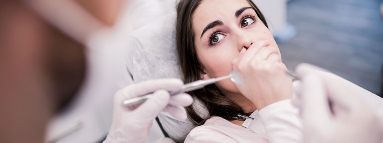 Frau sitzt beim Zahnarzt auf Behandlungsstuhl und hält sich den Mund zu