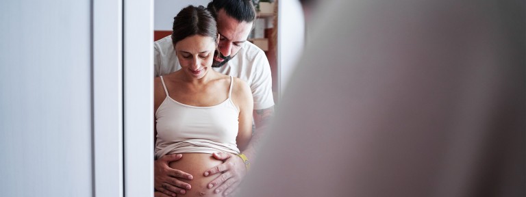 Mann hält schwangerer Frau vor sich den Bauch
