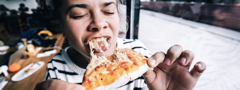 Junge Frau beißt herzhaft von einem Stück Pizza ab