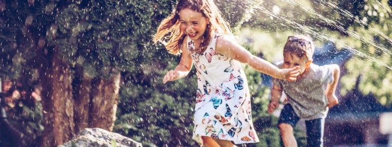 Mädchen und Junge rennen lachend durch Wasserstrahl