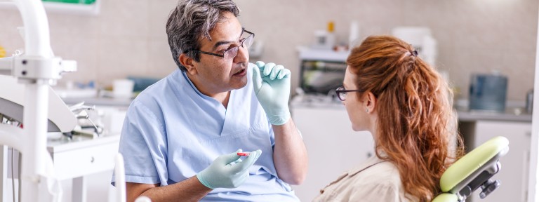 Zahnarzt erklärt rothaariger Frau auf Behandlungsstuhl etwas