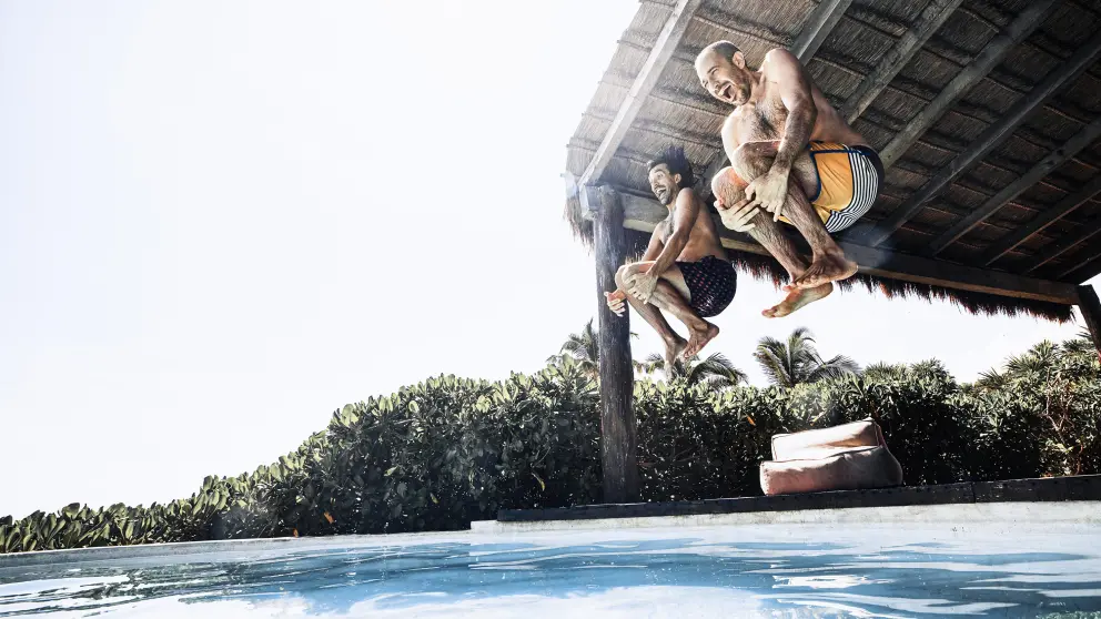 2 Männer springen mit angezogenen Knien in einen Pool