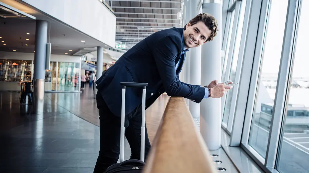 Mann im Anzug steht mit Koffer am Flughafen in einer Wartehalle