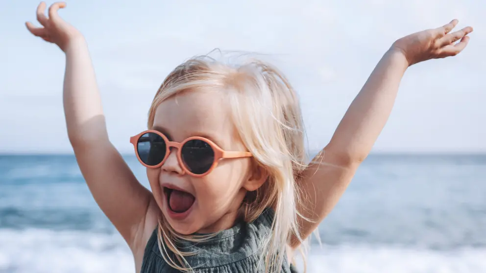 Junges Mädchen mit Sonnenbrille streckt lachend die Arme in die Luft