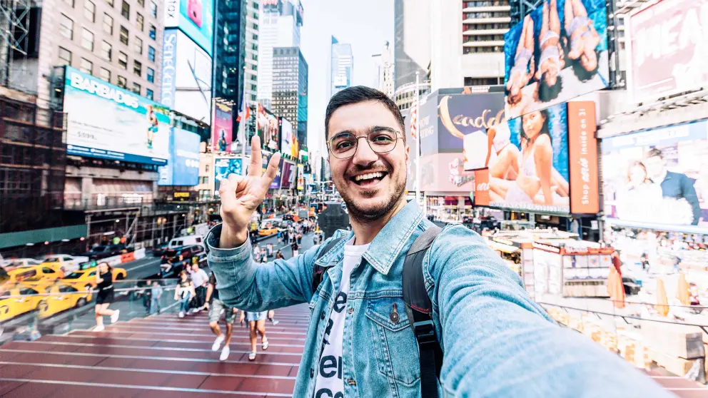 Mann mit Brille steht am Times Square und macht ein Selfie