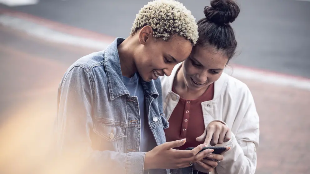 2 junge Frauen blicken gemeinsam lachend in ein Smartphone