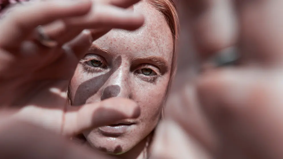 Frau mit Sommersprossen schaut durch ihre eigene Hand
