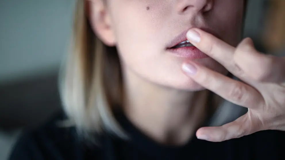 Junge Frau betatstet an ihrer Lippe ein Herpesblässchen