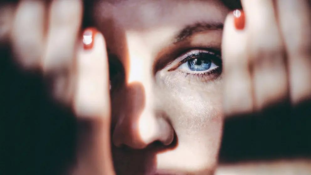 Junge Frau hält sich beide Hände vor das Gesicht und blickt mit einem Auge dazwischen durch
