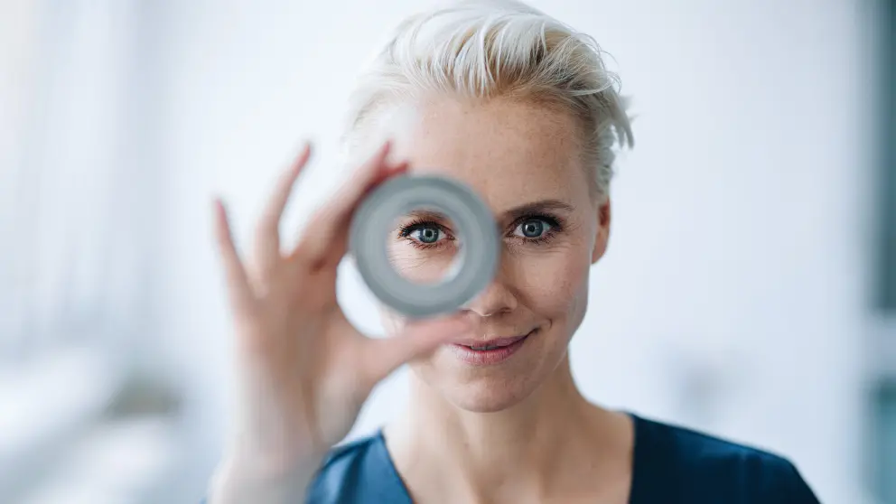 Frau hält eine Rolle vor ihr Gesicht und schaut mit einem Auge durch