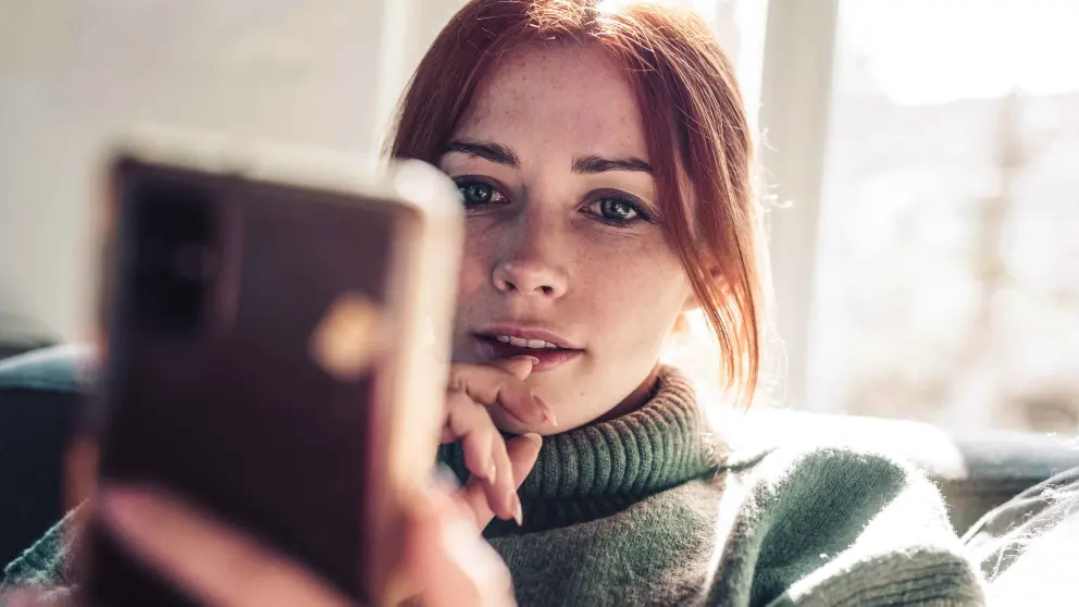 Junge rothaarige Frau schaut auf ihr Smartphone