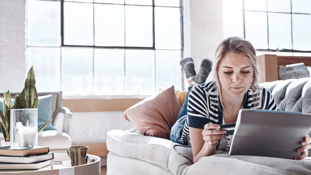 Junge Frau liegt auf Couch und arbeitet am Tablet