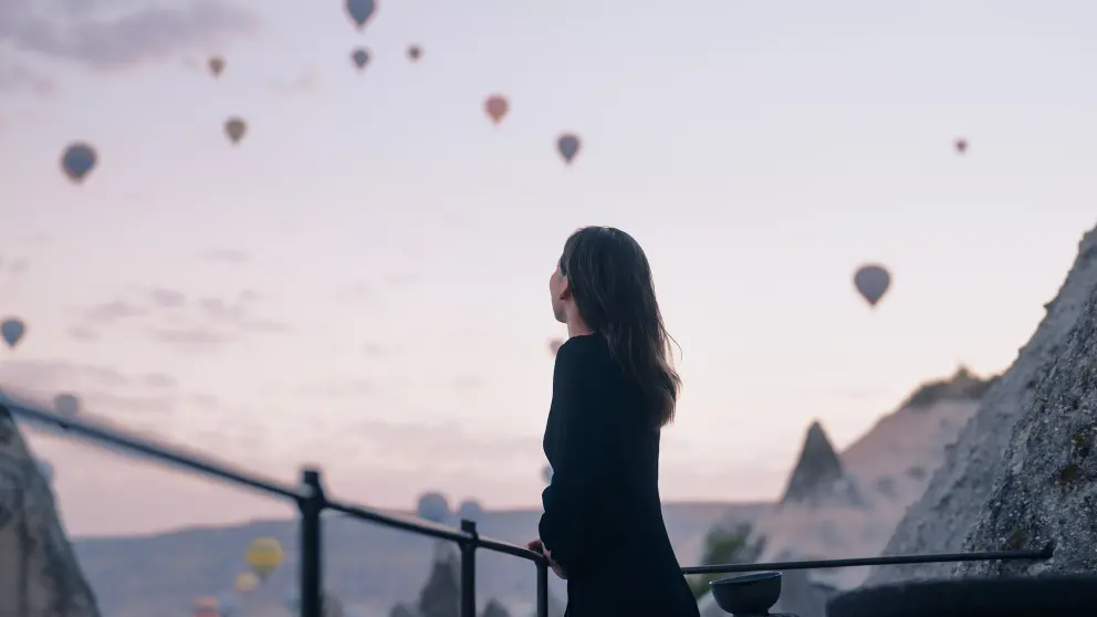 Frau blickt von Berg hinab und sieht einige Heißluftballons am Himmel