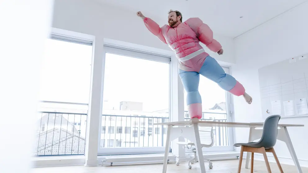 Mann in pinkem Kostüm steht als Superheld auf einem Tisch