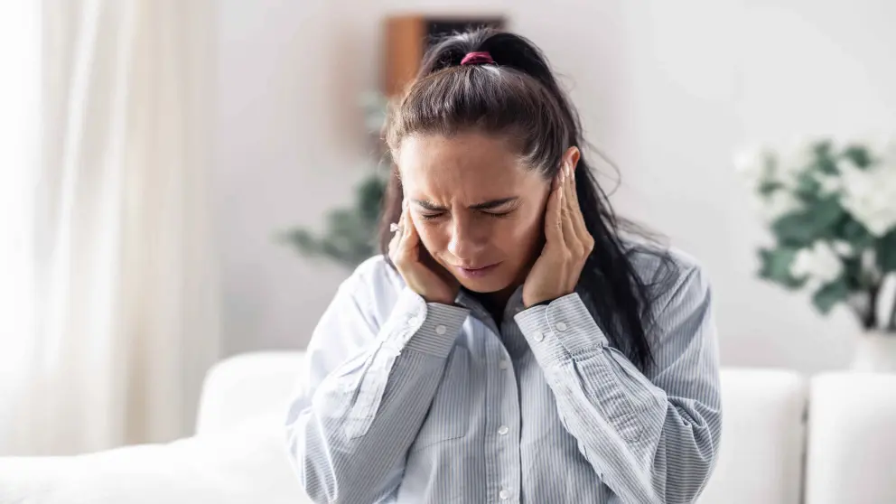 Junge Frau mit roten Haaren und vielen Sommersprossen hält sich mit beiden Händen die Ohren zu