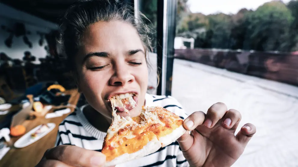 Junge Frau beißt herzhaft von einem Stück Pizza ab