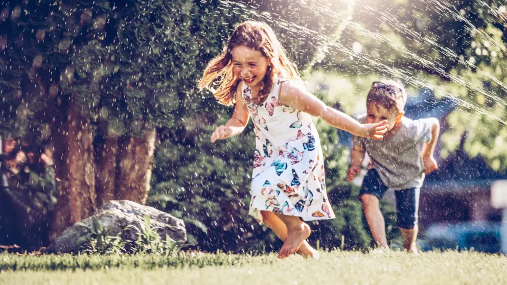 Mädchen und Junge rennen lachend durch Wasserstrahl