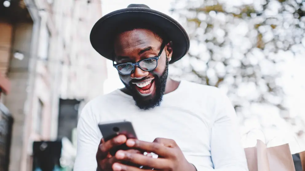 Mann mit Hut und Brille lacht in sein Smartphone