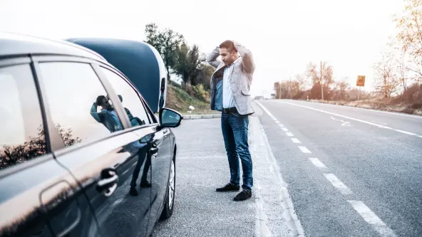 Mann hält seine Hände über den Kopf und steht vor seinem E-Auto neben einer Straße