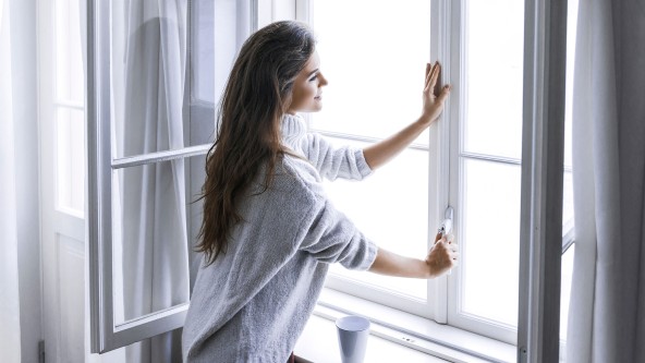 Frau mit langen braunen Haaren schließt ein Fenster