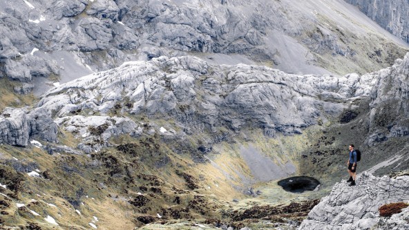 Mann steht in einer Senke in einem beeindruckenden Bergpanorama