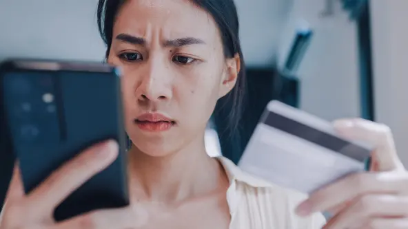 Frau hält mit einem kritischen Blick eine EC-Karte und ein Handy in ihren Händen
