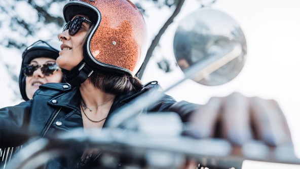 2 Frauen sitzen mit Helm und Sonnenbrille auf einem Motorrad