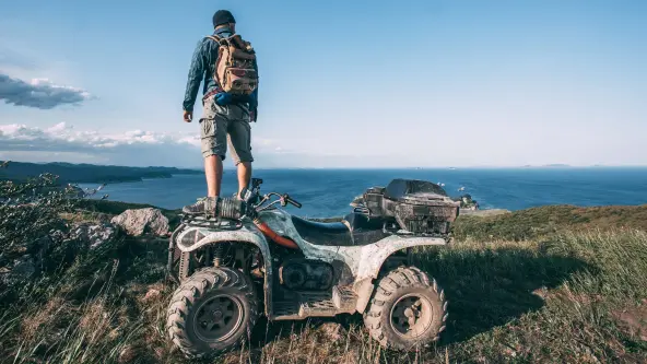 Mann steht mit Rucksack auf seinem verschmutzten Quad