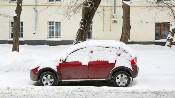 Rotes Auto auf einem zugeschneiten Parkplatz