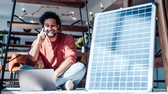 Mann sitzt neben einem großen Solarmodul und telefoniert lachend
