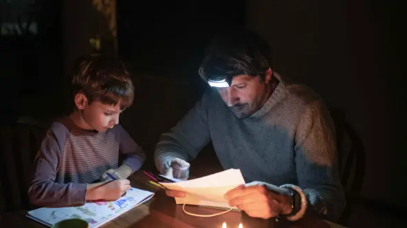 Vater und Sohn sitzen gemeinsam am Tisch mit einer Taschenlampe im Dunkeln