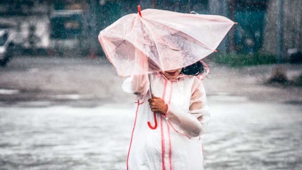 Frau mit rosa Jacke und rosa Regenschirm im Regen