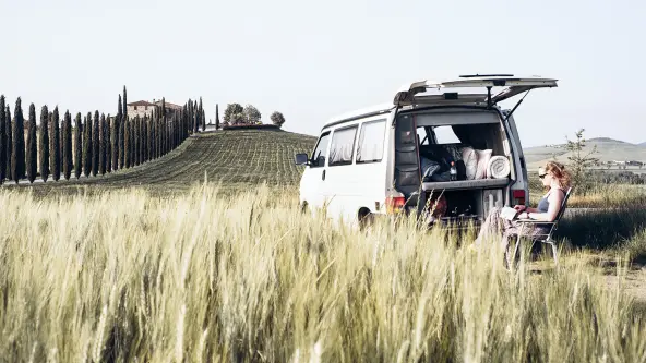 Mann sitzt auf Campingstuhl im Feld hinter seinem Camper