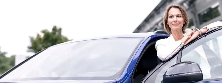Frau mittleren Alters steht vor blauem Auto