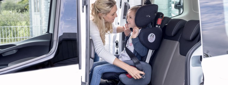 Mutter schnallt Mädchen im Autositz auf Rücksitzbank an