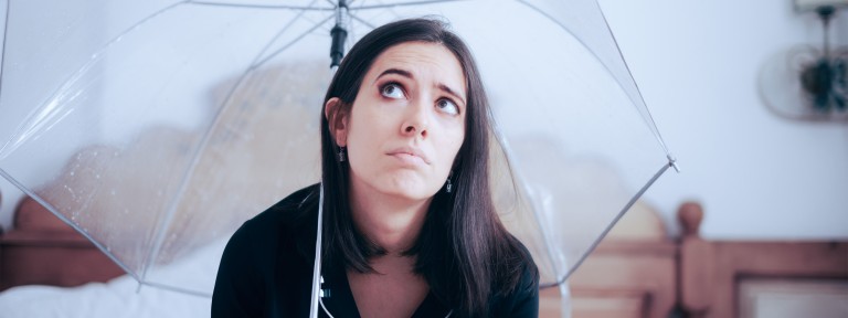 Junge Frau sitzt in Wohnung unter einem Regenschirm