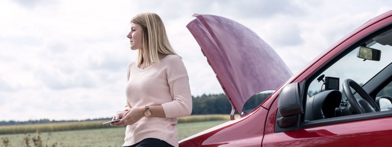 Junge Frau lehnt an ihrem defekten Auto
