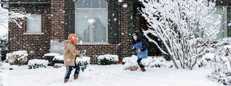 Zwei Kinder machen eine Schneeballschlacht vor einem Haus während es schneit