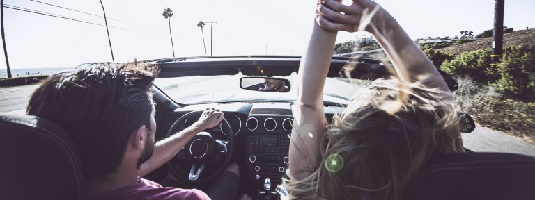 Mann fährt Cabrio während Frau auf Beifahrersitz Hände in die Luft streckt