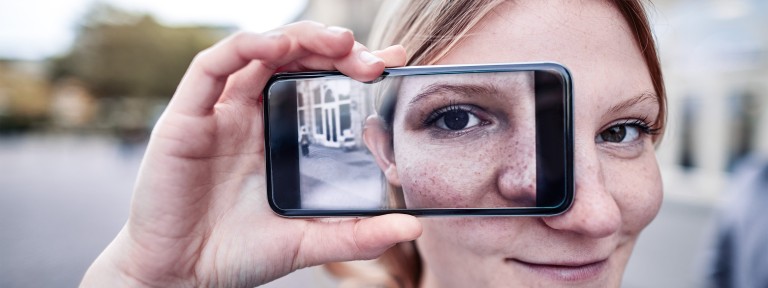 Frau hält sich Smartphone vor ihr Auge, welches wiederum auf dem Smartphone zu sehen ist