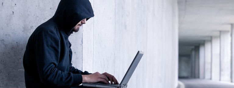 Mann in dunklem Kapuzen-Pullover arbeitet an einem Laptop auf seinem Schoß