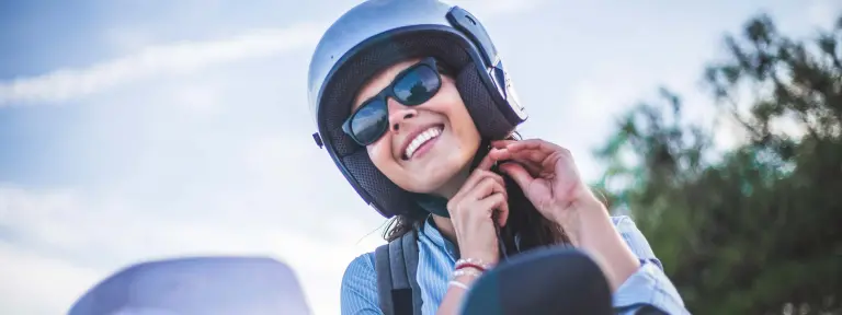 Frau mit Sonnenbrille schließt ihren Helm und sitzt auf einem Roller