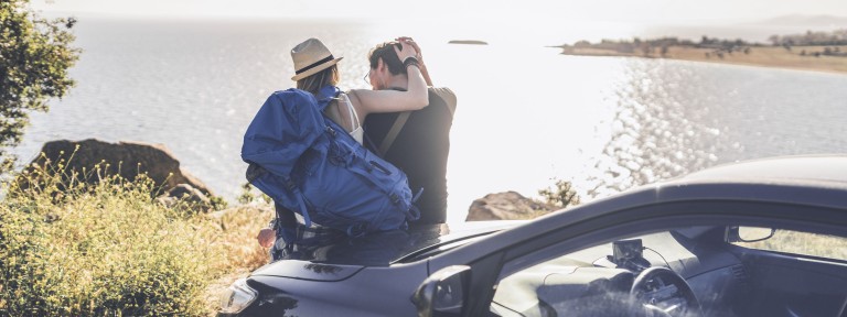 Paar sitzt auf ihrem Auto und blickt aufs Meer