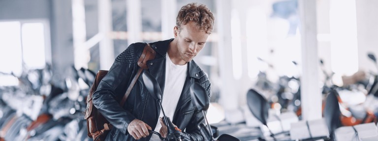 Junger Mann in schwarzer Lederjacke schaut sich Motorrad in einem Geschäft an