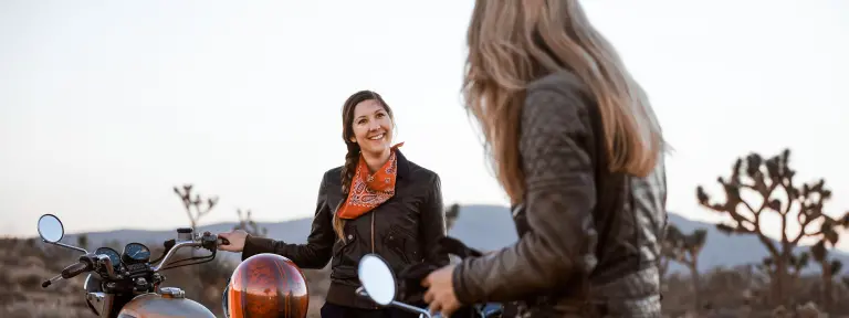 2 Frauen in Lederjacke lachen sich neben ihren Motorrädern an